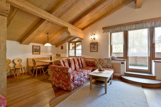 Wohnbereich Appartement Wilder Kaiser Wohnbereich einer Almhütte mit gemustertem Sofa, Holztisch und sichtbaren Dachbalken.