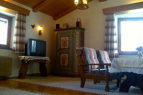 Rustikales Wohnzimmer mit Holzmöbeln, bemaltem Schrank, Fernseher und gepolsterten Sesseln.