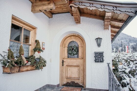 Eingang Haus Gantschnigg im Winter Eingangsbereich eines alpinen Hauses mit Holztür, Fensterkasten und winterlicher Dekoration.