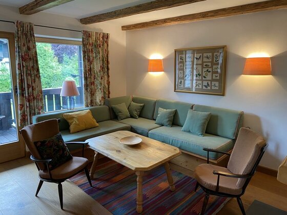 Wohnbereich Ferienwohnung Schmachtl Wohnzimmer mit grünem Ecksofa, Holztisch, zwei Sesseln und Deckenbalken aus Holz.