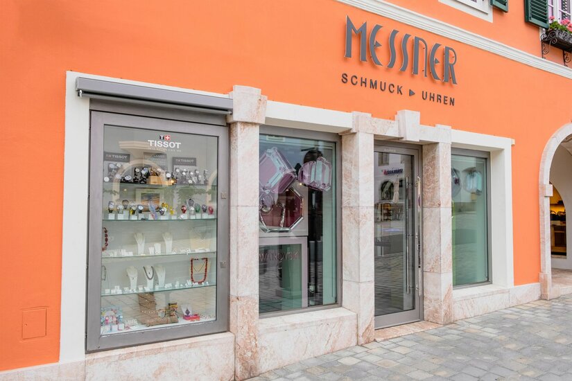 Außenansicht eines Schmuck- und Uhrengeschäfts mit orangefarbener Fassade und Schaufensterauslagen.