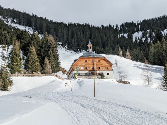 Bochumer Hütte in verschneiter Berglandschaft mit Nadelwald im Hintergrund.