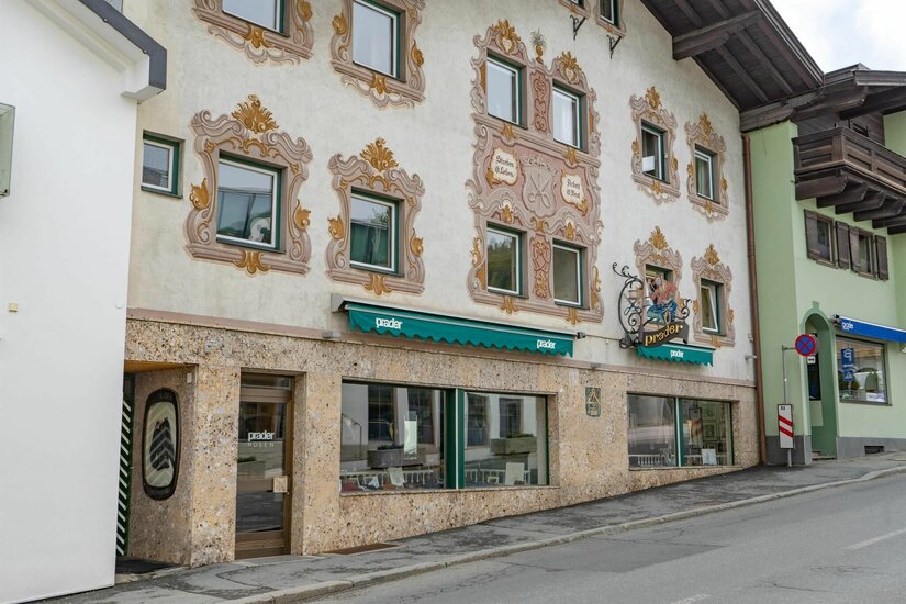Modehaus Prader Fassade eines Gebäudes mit Wandmalereien um die Fenster und einem Ladengeschäft im Erdgeschoss.