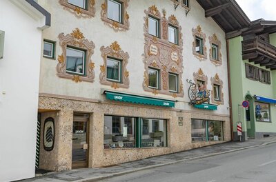 Fassade eines Gebäudes mit Wandmalereien um die Fenster und einem Ladengeschäft im Erdgeschoss.