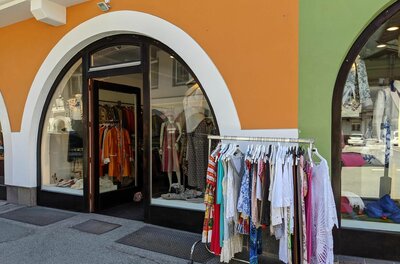 Modeboutique Jastella Eingangsbereich eines Modegeschäfts mit Rundbogenfenstern und Kleiderständer im Freien.