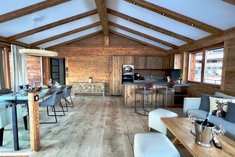 Innenansicht Hideaway Design Chalet Moderner Wohn- und Essbereich in einem Holzchalet mit offener Küche und Sichtbalken am Dach.