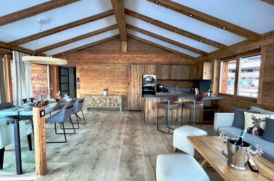 Moderner Wohn- und Essbereich in einem Holzchalet mit offener Küche und Sichtbalken am Dach.