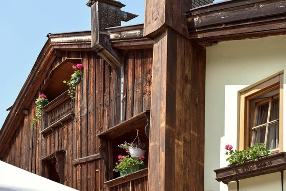 Fassade Gasthof Alte Wacht Nahaufnahme einer Holzfassade mit Blumenkästen an Fenstern und Balkonen.