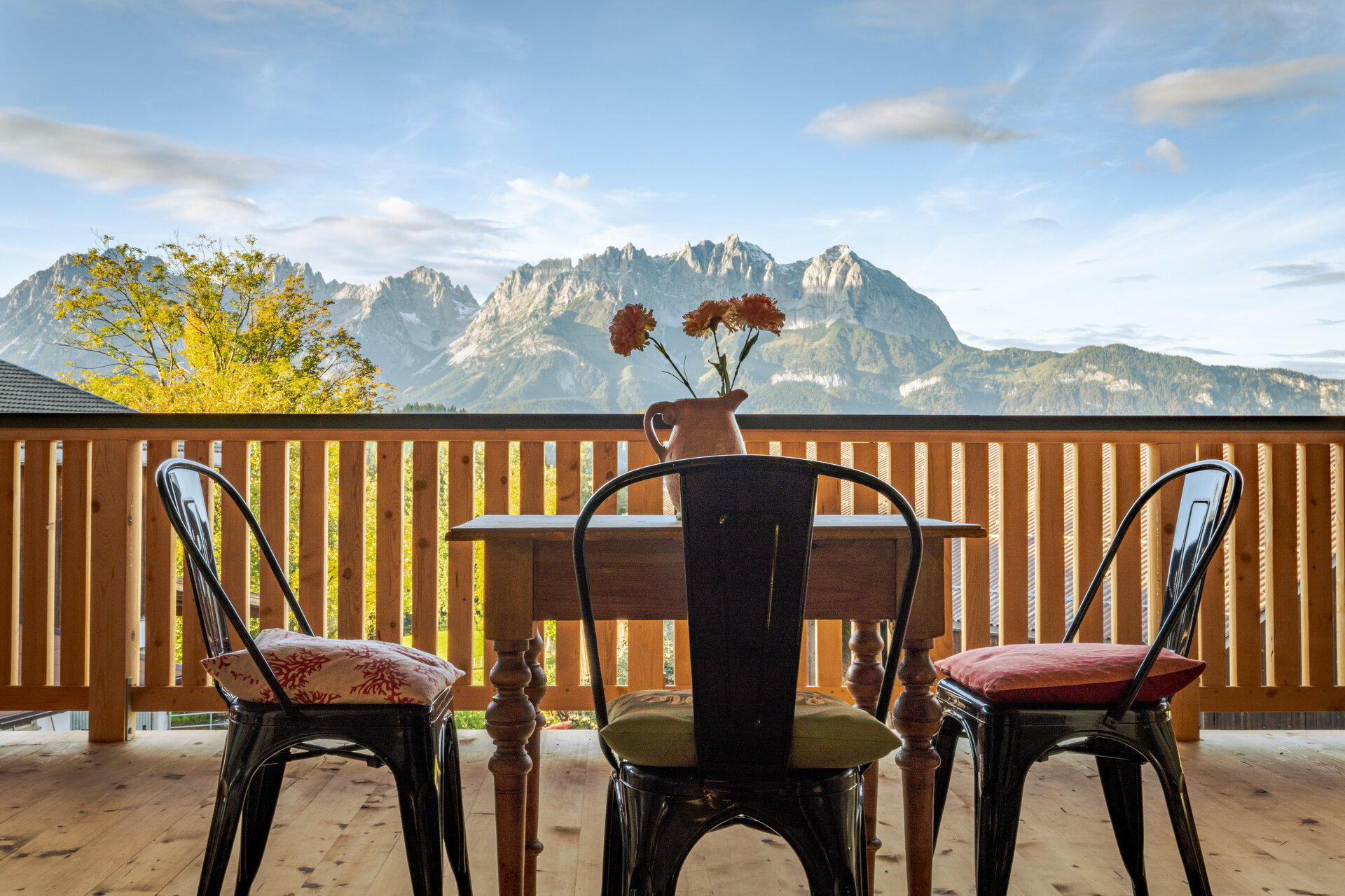 Der Blick von einem Holz-Balkon in Kitzbühel auf das Bergmassiv des Wilden Kaisers, mit einem Tisch und Stühlen, die zum Entspannen einladen.