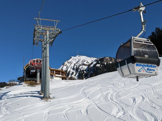 Gondelbahn am Kitzbüheler Horn Gondel der Kitzbüheler Hornbahn über einer verschneiten Skipiste vor blauem Himmel.