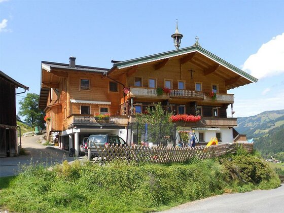 Ein mehrstöckiges Holzhaus im alpinen Stil mit Balkonen, Blumenschmuck und einem kleinen Spielplatz davor.