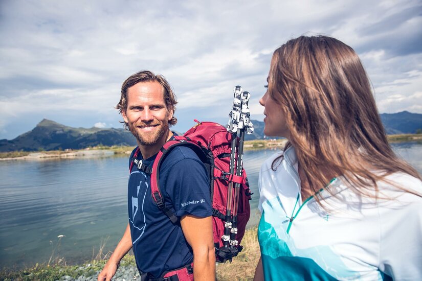 Zwei Wanderer mit Rucksäcken und Wanderstöcken vor einem Bergsee.