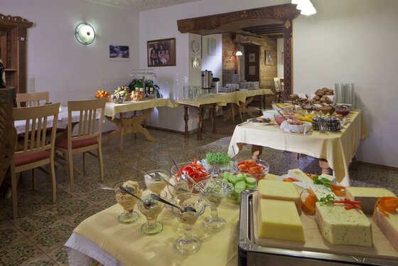 Frühstücksbuffet mit Käseplatten, Aufstrichen und frischem Gemüse in einem rustikalen Speisesaal.