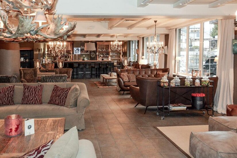 Lounge & Bar Maria Theresia Lounge-Bereich mit Ledersofas, Kronleuchtern aus Geweih und einer Bar im Hintergrund.