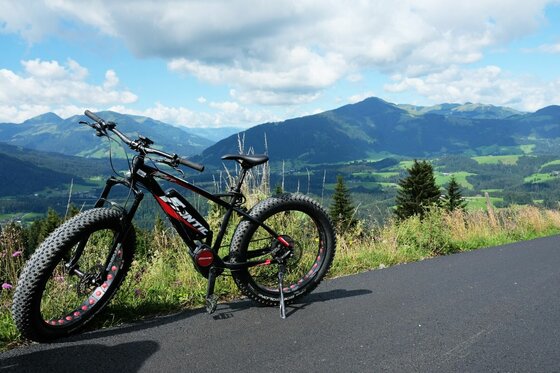 Ein schwarzes E-Fatbike steht auf einer asphaltierten Straße vor einem Bergpanorama.