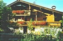 Haus Scherler im Sommer Mehrstöckiges Holzhaus mit Balkonen und Blumenschmuck unter blauem Himmel.