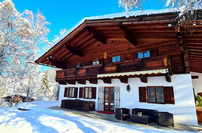 Villa Alpenblick im Winter Alpines Holzhaus mit weißer Fassade in einer verschneiten Winterlandschaft unter blauem Himmel.