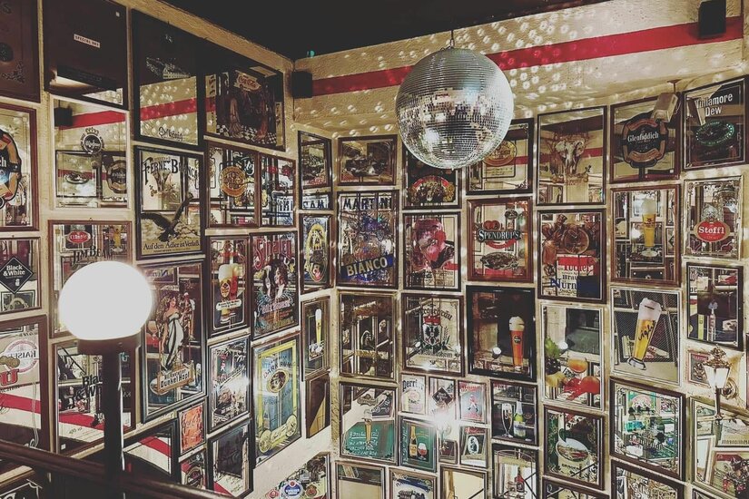 Lichtl Musicbar Innenansicht Innenansicht einer Bar mit vielen gerahmten Werbeplakaten an den Wänden und einer Discokugel an der Decke.