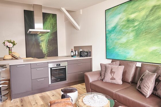 Wohnküche Kitzhome City Apartments Moderne Küchenzeile mit Einbaubackofen neben einem braunen Ledersofa und großformatigen Wandbildern.
