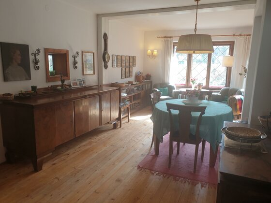 Wohn- und Essbereich mit Holzboden, rundem Esstisch, dunklem Sideboard und Wandbildern.