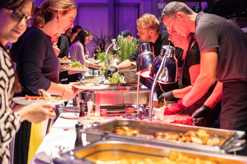 Genusscatering Ein Buffet mit verschiedenen Gerichten wird von mehreren Personen präsentiert. Gäste wählen aus einer Vielzahl von Speisen und genießen das Essen in einer festlichen Atmosphäre.