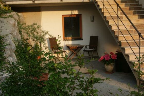 Gepflasterte Terrasse mit Holztisch, zwei Stühlen und einer Außentreppe aus Stein.