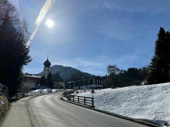 Straße nach Kochau Asphaltierte Straße führt an einer Kirche mit Zwiebelturm und schneebedeckten Hängen vorbei.