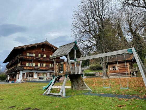 Spielplatz beim Hotel Vordergrub Holzspielplatz mit Kletterturm und Schaukel vor einem traditionellen Alpenhotel aus dunklem Holz.
