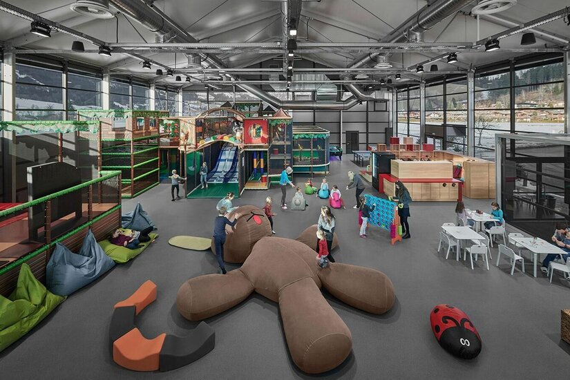 Großer Indoor-Spielplatz mit Klettergerüsten, Rutschen und Sitzsäcken in einer modernen Halle.