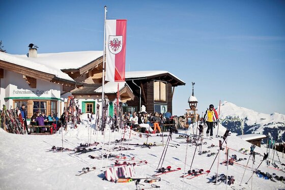 Hahnenkammstüberl im Winter Hahnenkammstüberl im Winter mit Skifahrern, Skiern im Schnee und Tiroler Flagge.