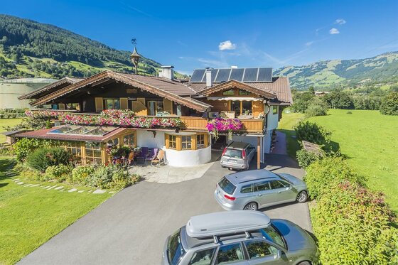 Alpines Landhaus mit Blumenschmuck, Parkplatz und Bergpanorama im Hintergrund.