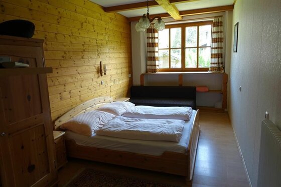 Schlafzimmer mit Doppelbett aus Holz, holzgetäfelter Wand und Fenster.