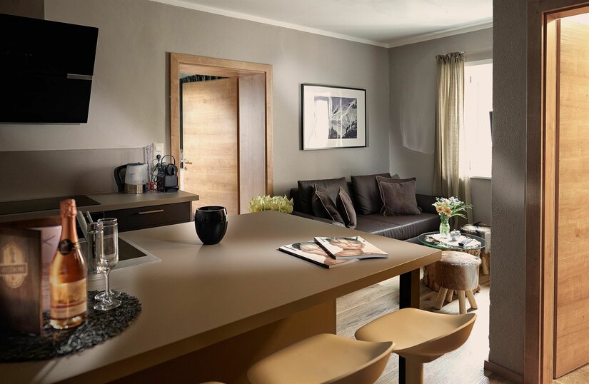 Wohnzimmer Kitzhome City Apartments Moderner Wohn- und Essbereich mit Küchentresen, Barhockern und dunklem Sofa.