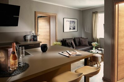 Wohnzimmer Kitzhome City Apartments Moderner Wohn- und Essbereich mit Küchentresen, Barhockern und dunklem Sofa.