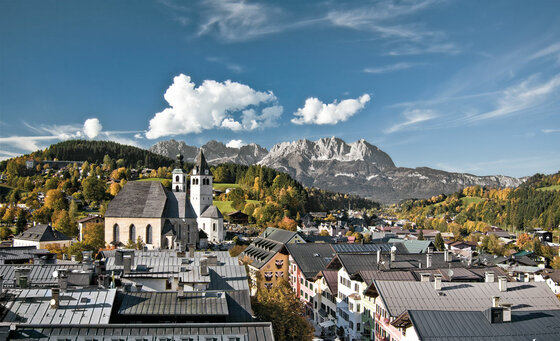 Blick über die Dächer von Kitzbühel mit der Stadtpfarrkirche und dem Wilden Kaiser im Hintergrund.