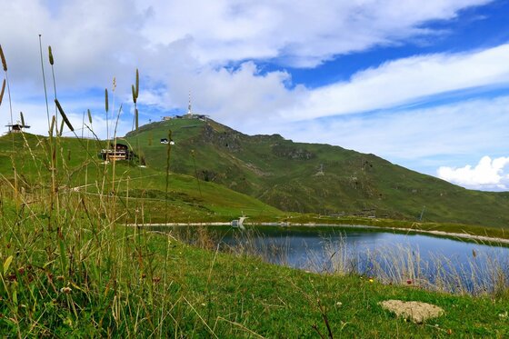 Ein Bergsee im Vordergrund mit Blick auf das Kitzbüheler Horn unter blauem Himmel.