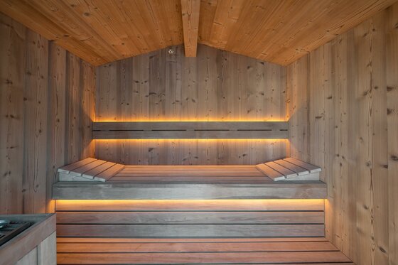 WEB_HansFrauenschuh_-51 Eine moderne Sauna mit Holzverkleidung und sanfter Beleuchtung. Die Sitzbänke sind aus Holz und laden zum Entspannen ein.