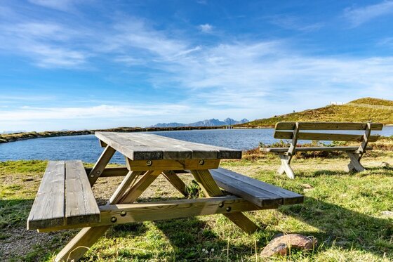 Holzpicknicktisch und eine Bank an einem Bergsee unter blauem Himmel.