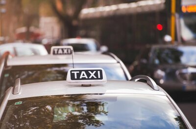 Nahaufnahme eines weißen Taxi-Schildes auf einem Autodach in einer Reihe wartender Fahrzeuge.