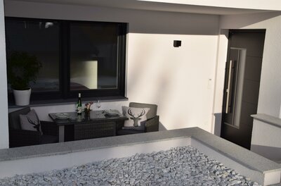 Moderne Terrasse mit Sitzgruppe, gedecktem Tisch und Kissen mit Hirschmotiv vor einer weißen Hauswand.