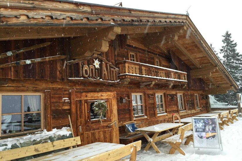 Toni Alm im Winter Rustikale Holzhütte mit Balkon und schneebedeckter Terrasse im Winter.