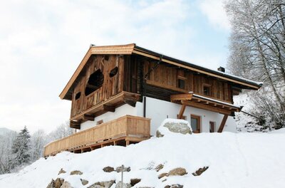 Ein charmantes Holzhaus in einer schneebedeckten Landschaft. Die Umgebung ist ruhig und malerisch, umgeben von Bäumen.