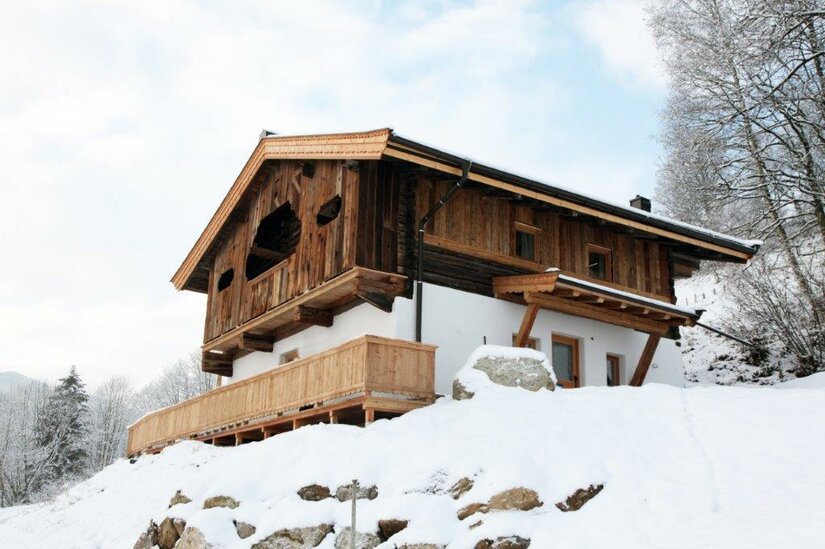 Ein charmantes Holzhaus in einer schneebedeckten Landschaft. Die Umgebung ist ruhig und malerisch, umgeben von Bäumen.