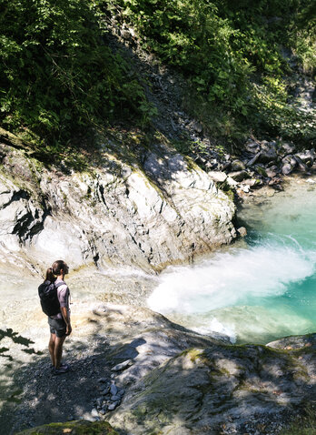 Eine Frau steht auf einem Felsen und schaut auf türkisgrünes Wasser unterhalb