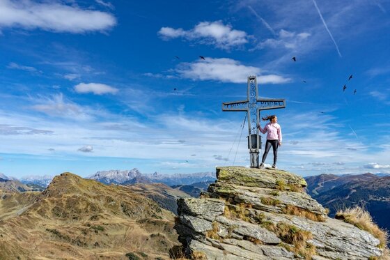 Gipfelkreuz in den Südbergen Person steht neben einem metallenen Gipfelkreuz auf einem felsigen Berggipfel vor Alpenpanorama.