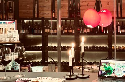 Weinherz Kitzbühel Innenansicht Zwei Gläser Rotwein auf einem Tisch vor einem Weinregal mit Kerzen und einem Tablet.