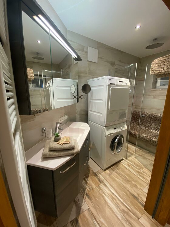 Ein modernes Badezimmer mit einer Waschmaschine und einem Trockner. Das Design ist hell und freundlich mit Holzfliesen und einer eleganten Waschtischkombination.
