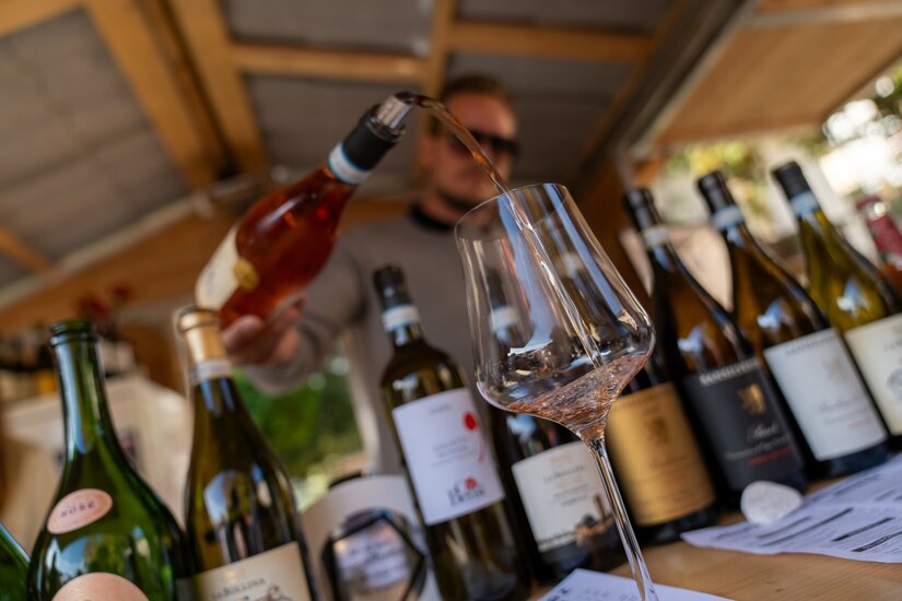 Ein Mann schenkt Roséwein aus einer Flasche in ein Weinglas ein, umgeben von weiteren Weinflaschen.
