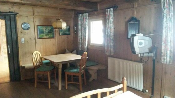 Sitzecke im Angererhof Rustikale Sitzecke aus Holz mit Tisch, zwei Stühlen, Eckbank und einem kleinen Fernseher an der Wand.