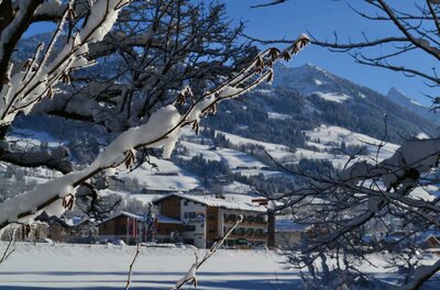Hotel Aurach im Winter Verschneite Äste im Vordergrund mit Blick auf das Hotel Aurach und winterliche Berge.